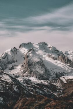 Snow-covered mountain range under cloudy sky Snowy mountain peaks with cloudy sky